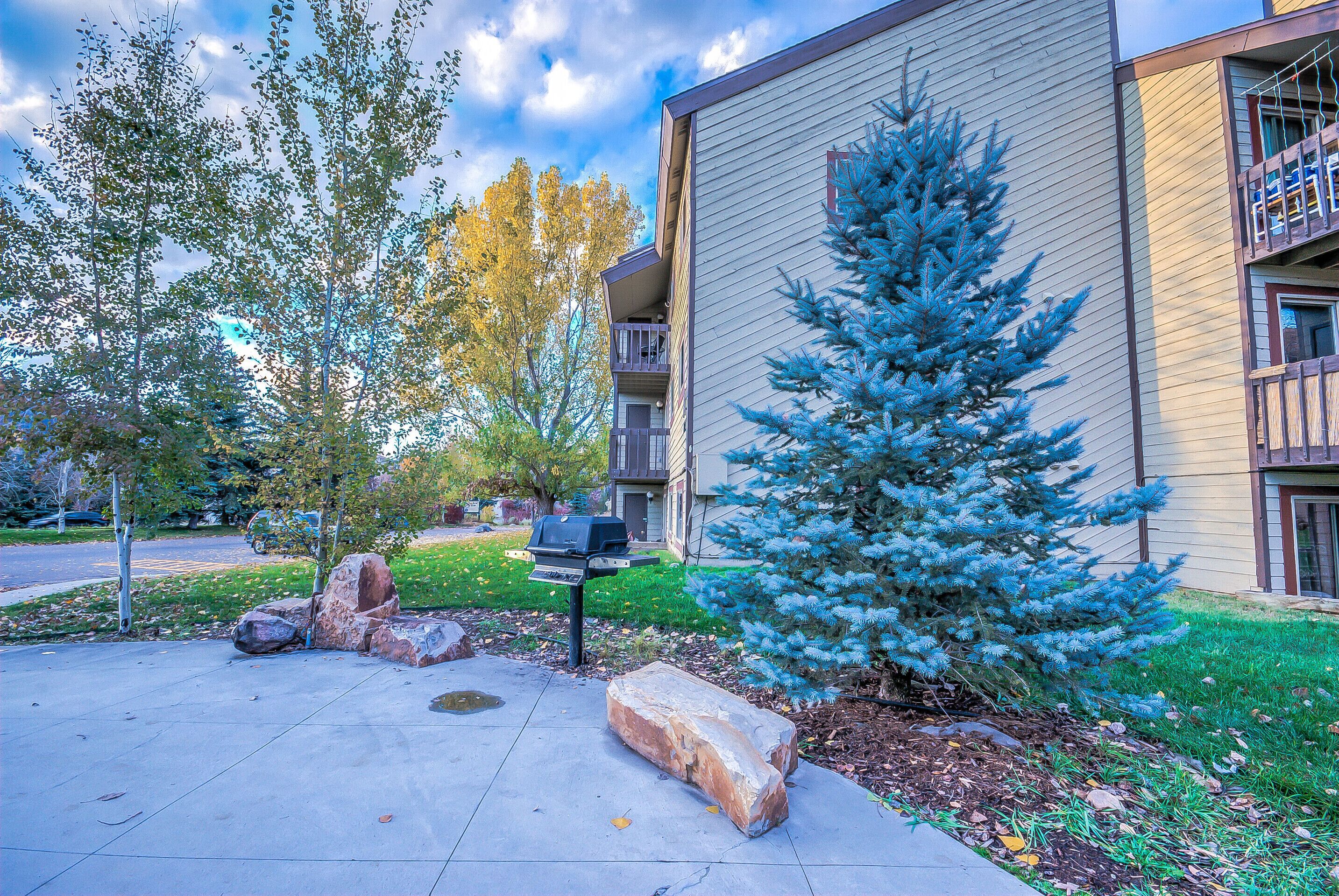 A residential building with a balcony, a small tree, and a barbecue grill in the yard.
