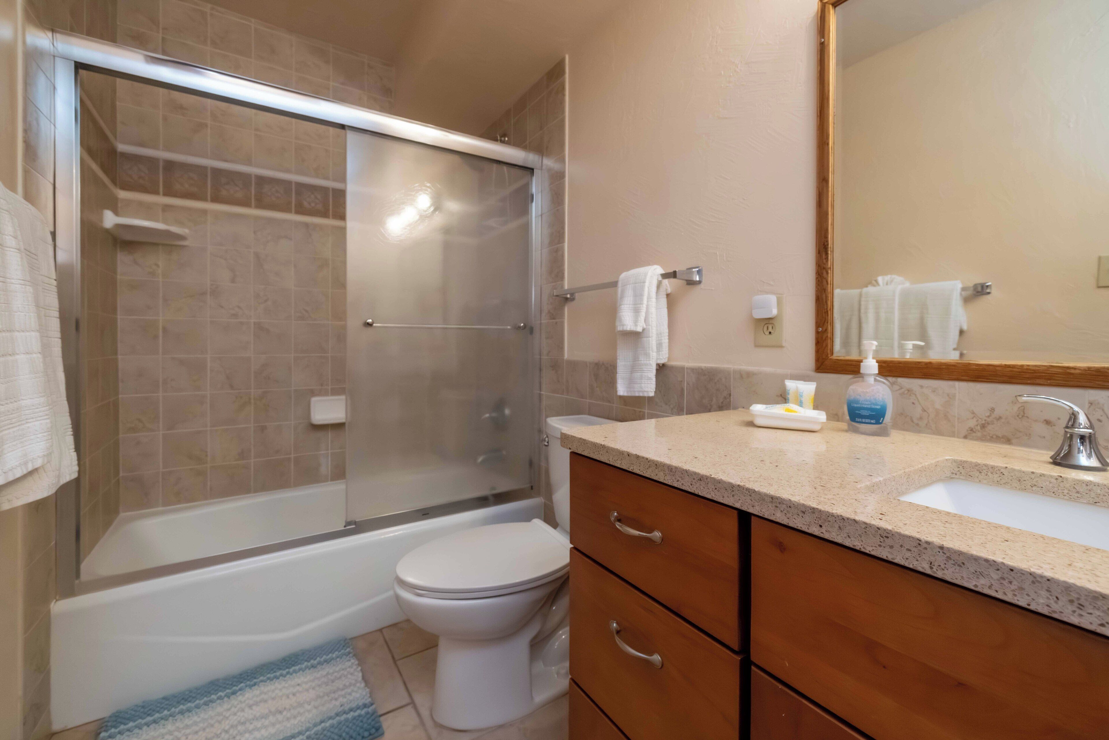 A bathroom with a glass-enclosed shower, a toilet, a sink with a mirror, and wooden cabinets.