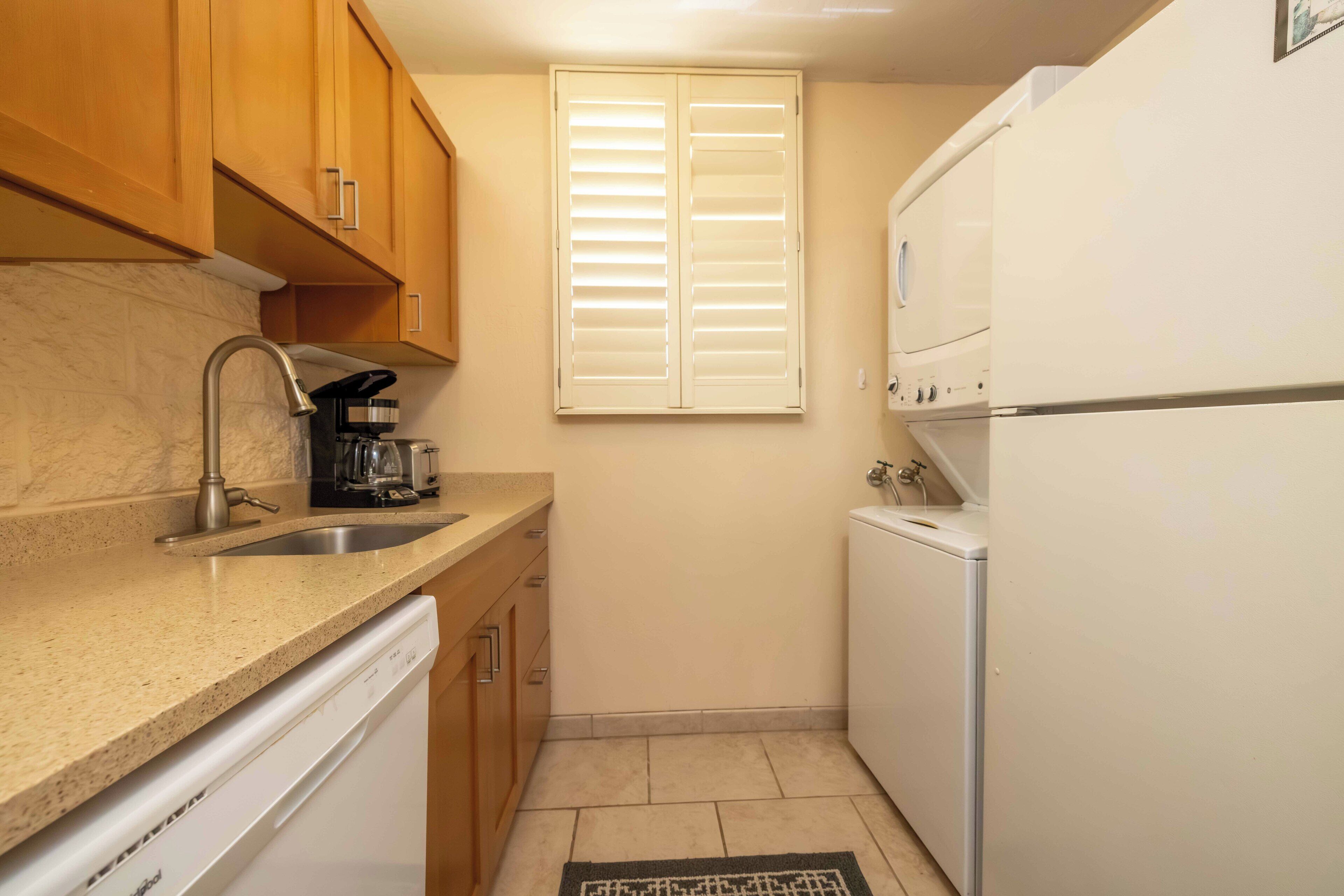 Cocina compacta con armarios de madera, un lavamanos de acero inoxidable, lavavajillas y refrigerador blanco.