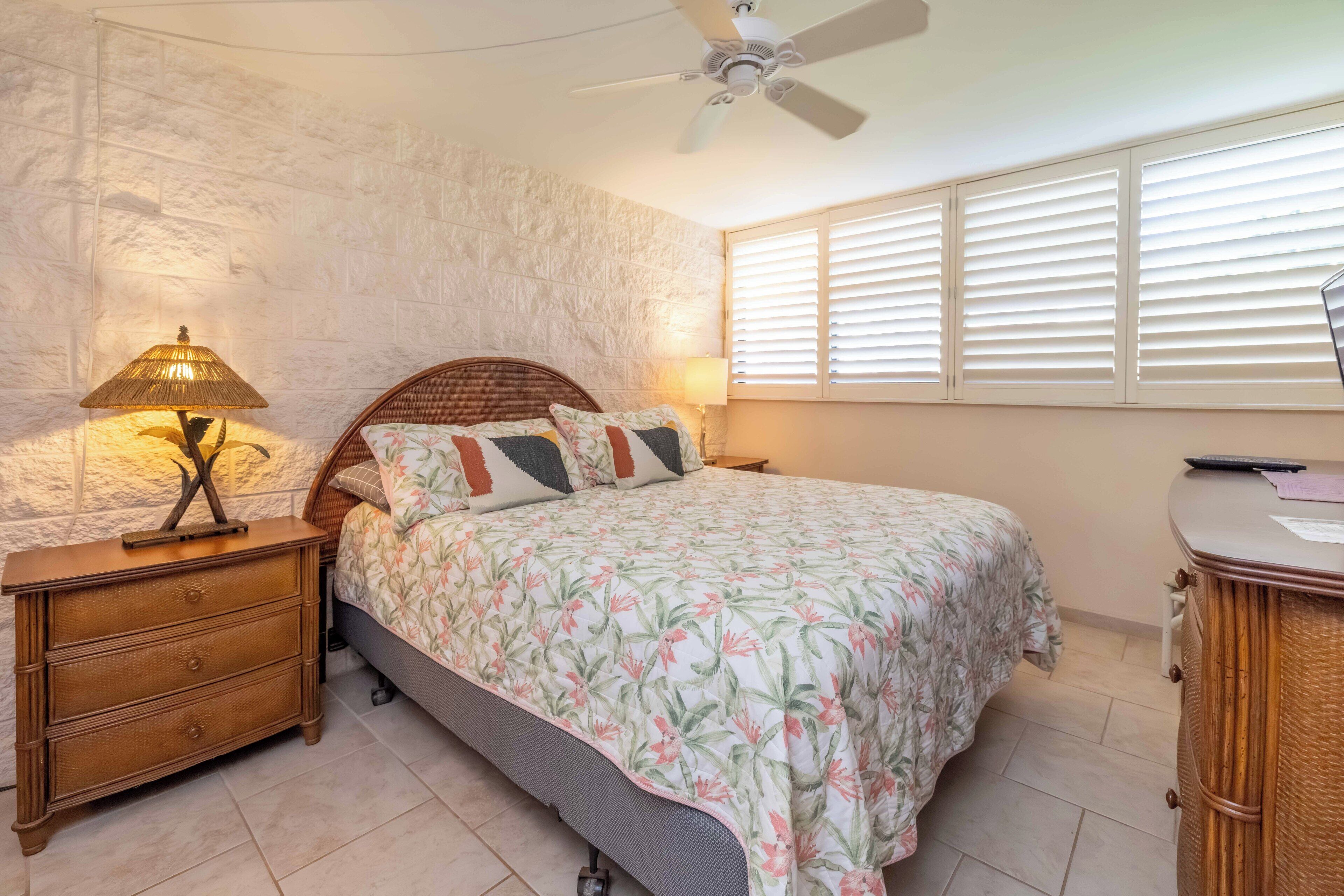 Un dormitorio con cama, mesita de noche, lámpara y ventilador de techo.