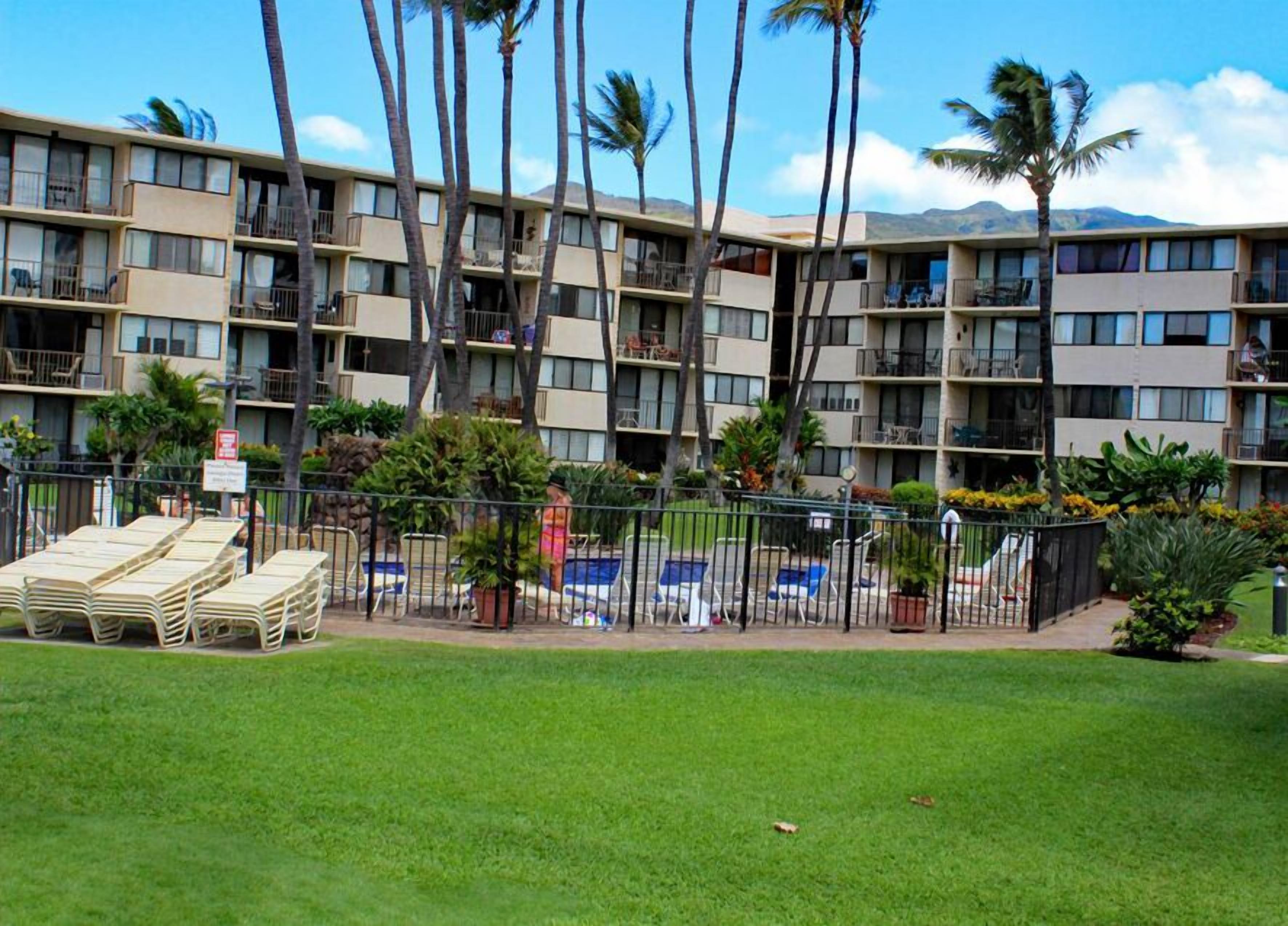 A multi-story hotel with balconies, a swimming pool, and palm trees.
