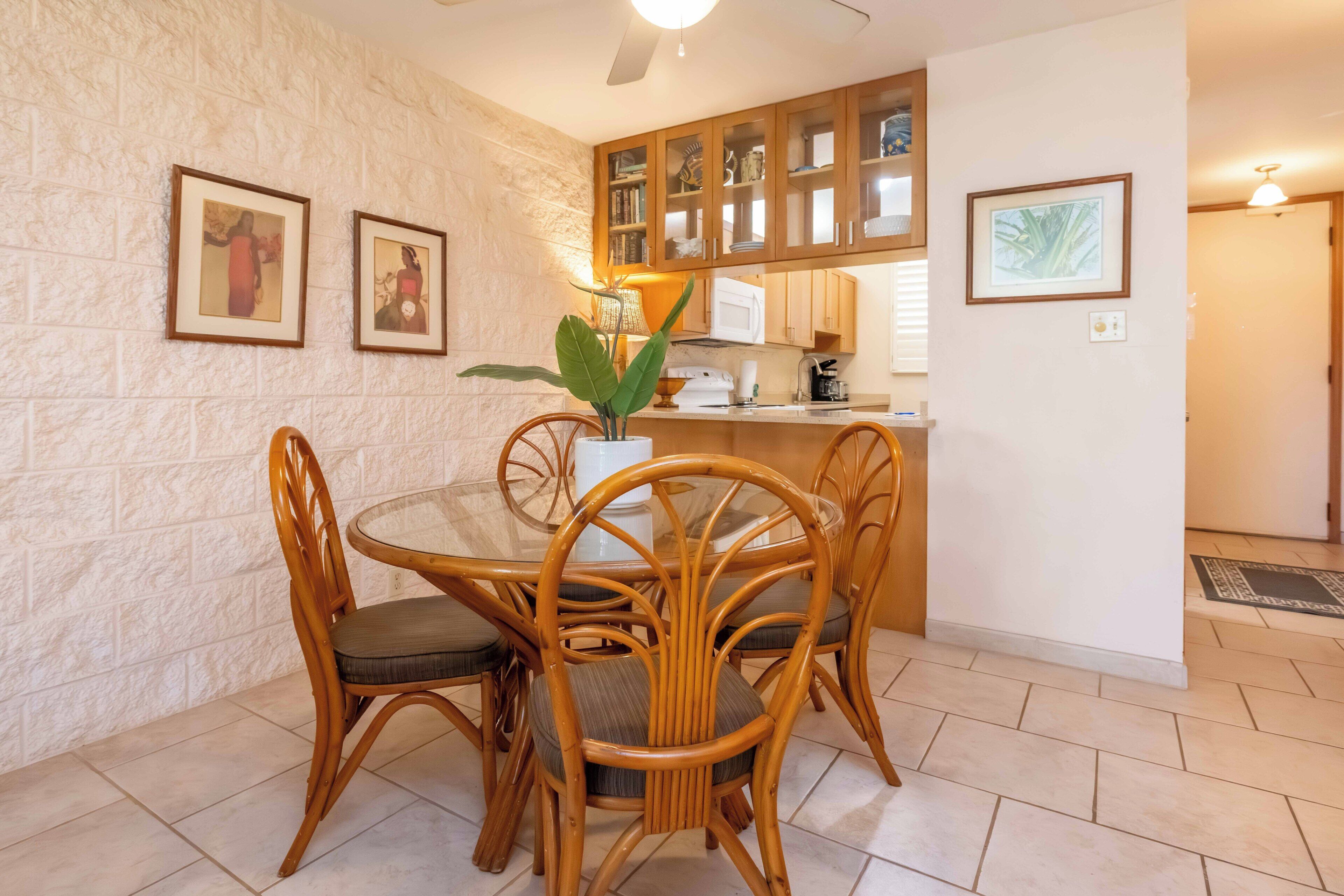 A dining area with a round table and wicker chairs, a kitchen with wooden cabinets, and framed artwork on the walls.