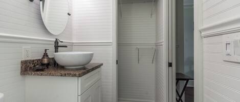A bathroom with a white vanity, a large mirror, a sink, and a shower area.