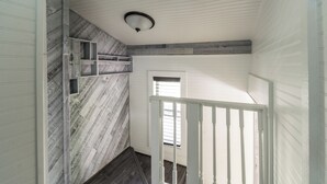 A hallway with a sloped ceiling, a white railing, and a window with blinds. - Pet friendly studio on 2nd level with a full bathroom and kitchen (Gainesville)