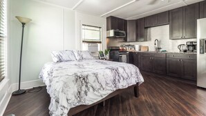 A bedroom with a bed, a standing lamp, and a view of the kitchen. - Pet friendly studio on 2nd level with a full bathroom and kitchen (Gainesville)
