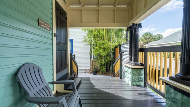 A porch with two Adirondack chairs, a wooden door, and a sign reading "Downtown Studio Depot Village". - Pet friendly studio on 2nd level with a full bathroom and kitchen (Gainesville)