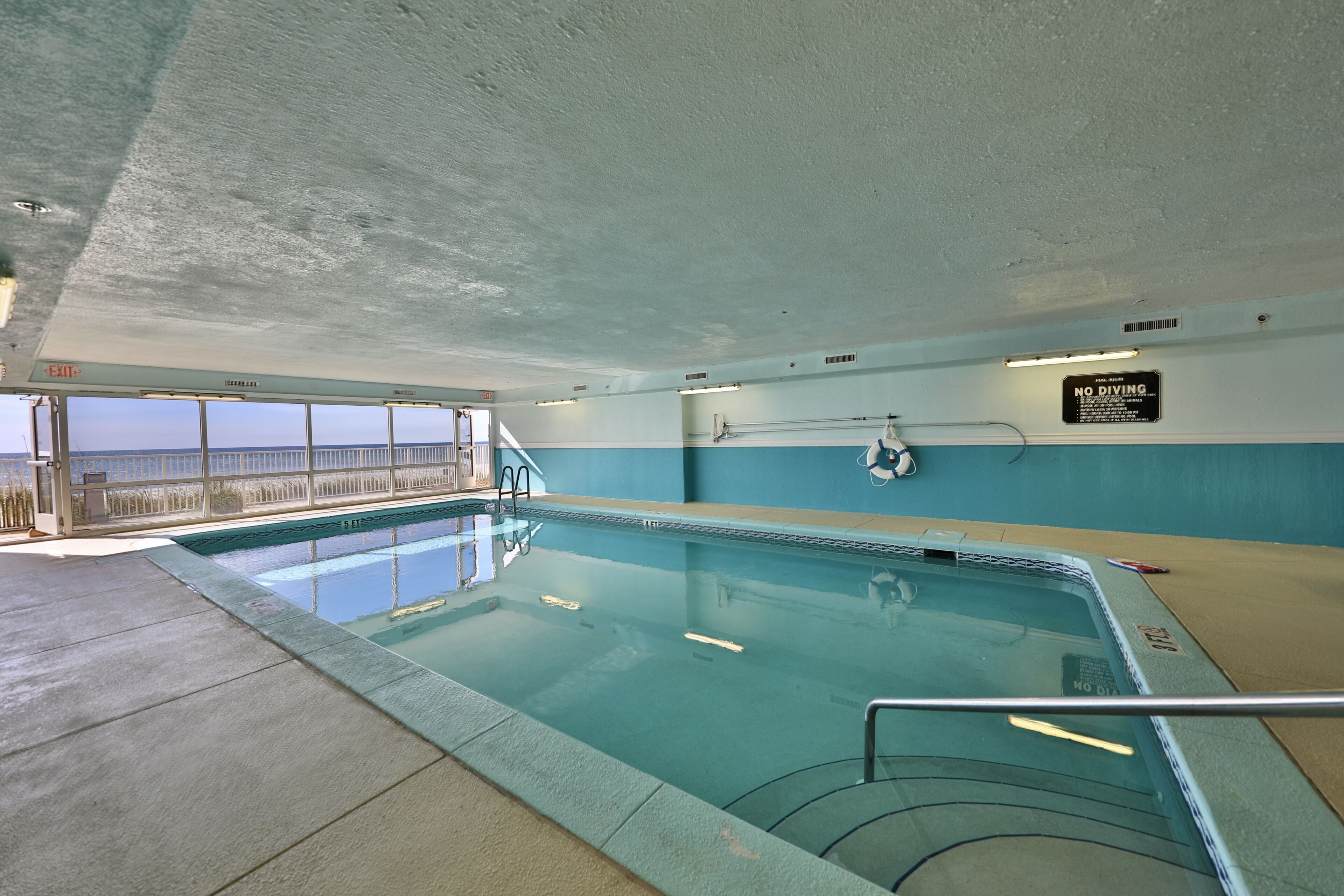 An indoor swimming pool with clear water, a lifebuoy, and a 'No Diving' sign.
