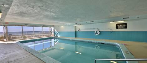 An indoor swimming pool with clear water, a lifebuoy, and a 'No Diving' sign.