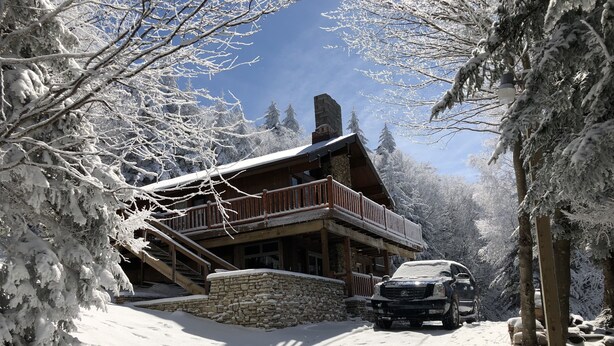 A snow-covered lodge with a stone foundation, wooden exterior, and a balcony overlooking the snowy landscape. - SLOPESIDE CHALET, Near the top of Shay's Revenge / Ski in-Ski out / Great Views  (Snowshoe)