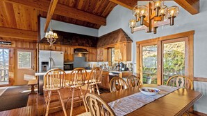 A wooden interior with a dining table, chairs, a chandelier, and a kitchen area. - SLOPESIDE CHALET, Near the top of Shay's Revenge / Ski in-Ski out / Great Views  (Snowshoe)