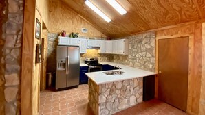 A compact kitchen with a stone accent wall, wooden ceiling, and a built-in island with a sink. - Waterfall Pool, Cabana, Mountain Views, Outdoor Fireplace, 3 Minutes 2 Frio! (Concan)