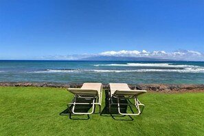 Dos sillones de descanso frente al océano, con vista despejada al mar y una cadena montañosa distante.