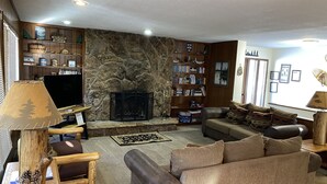 Uma sala de estar aconchegante com lareira de pedra, uma estante de livros, um sofá confortável e uma televisão.