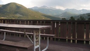 Um deck de madeira com uma mesa de piquenique, com vista para uma paisagem montanhosa com picos nevados.