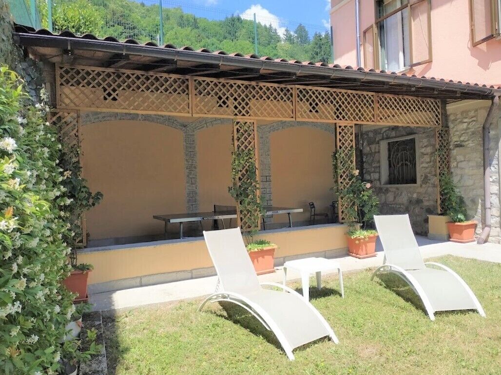 An outdoor seating area with two lounge chairs and a table, surrounded by potted plants and a stone wall.