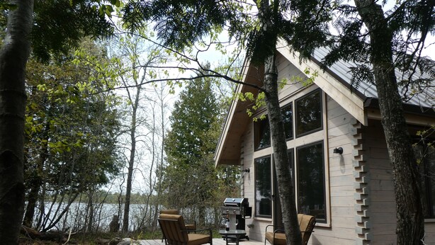 Une cabane avec une terrasse, un barbecue et vue sur le lac.