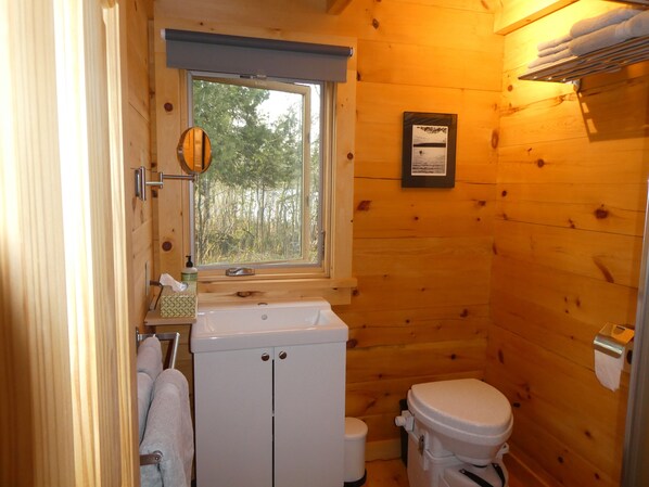Een kleine houten badkamer met een raam, een wastafel, een toilet en een handdoekhouder.