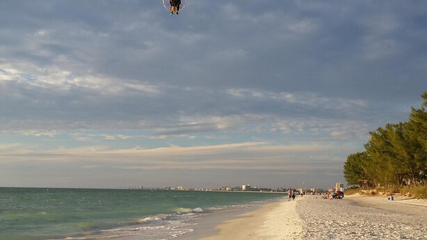 En strand med en parasail som svävar i luften, en sandstrand och havet i bakgrunden.