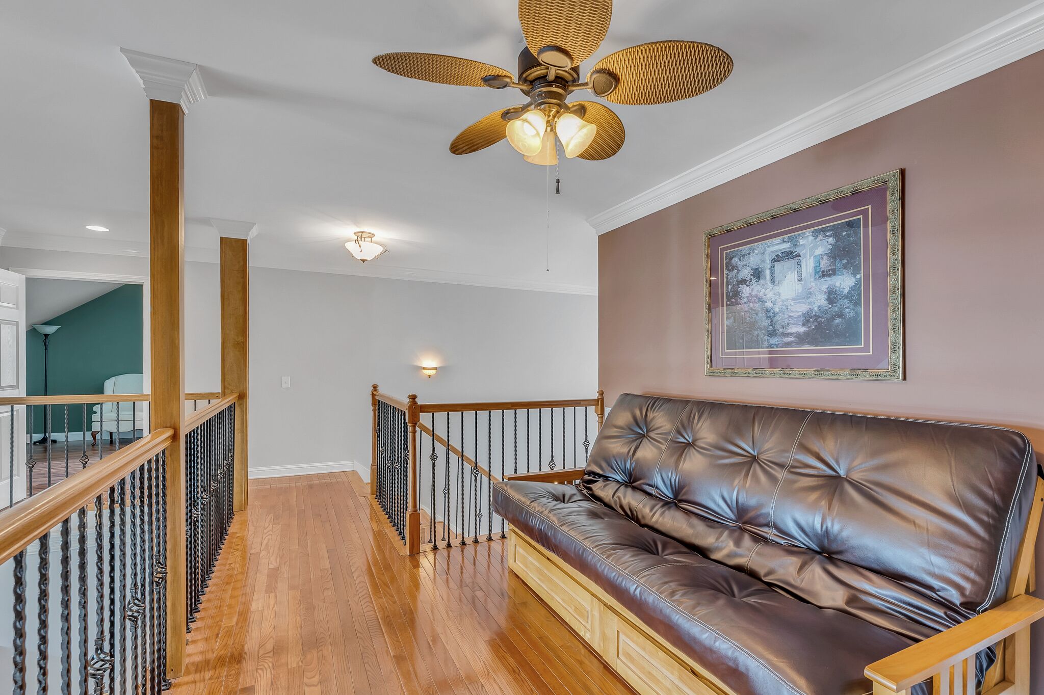 A modern living room with a leather sofa, wooden railing, and a ceiling fan.