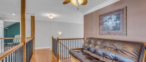A modern living room with a leather sofa, wooden railing, and a ceiling fan.