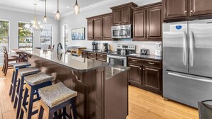 A modern kitchen with dark wood cabinets, stainless steel appliances, and a central island with bar stools. - Sandestin 4BR Villa | Golf Views + Pool (Miramar Beach)