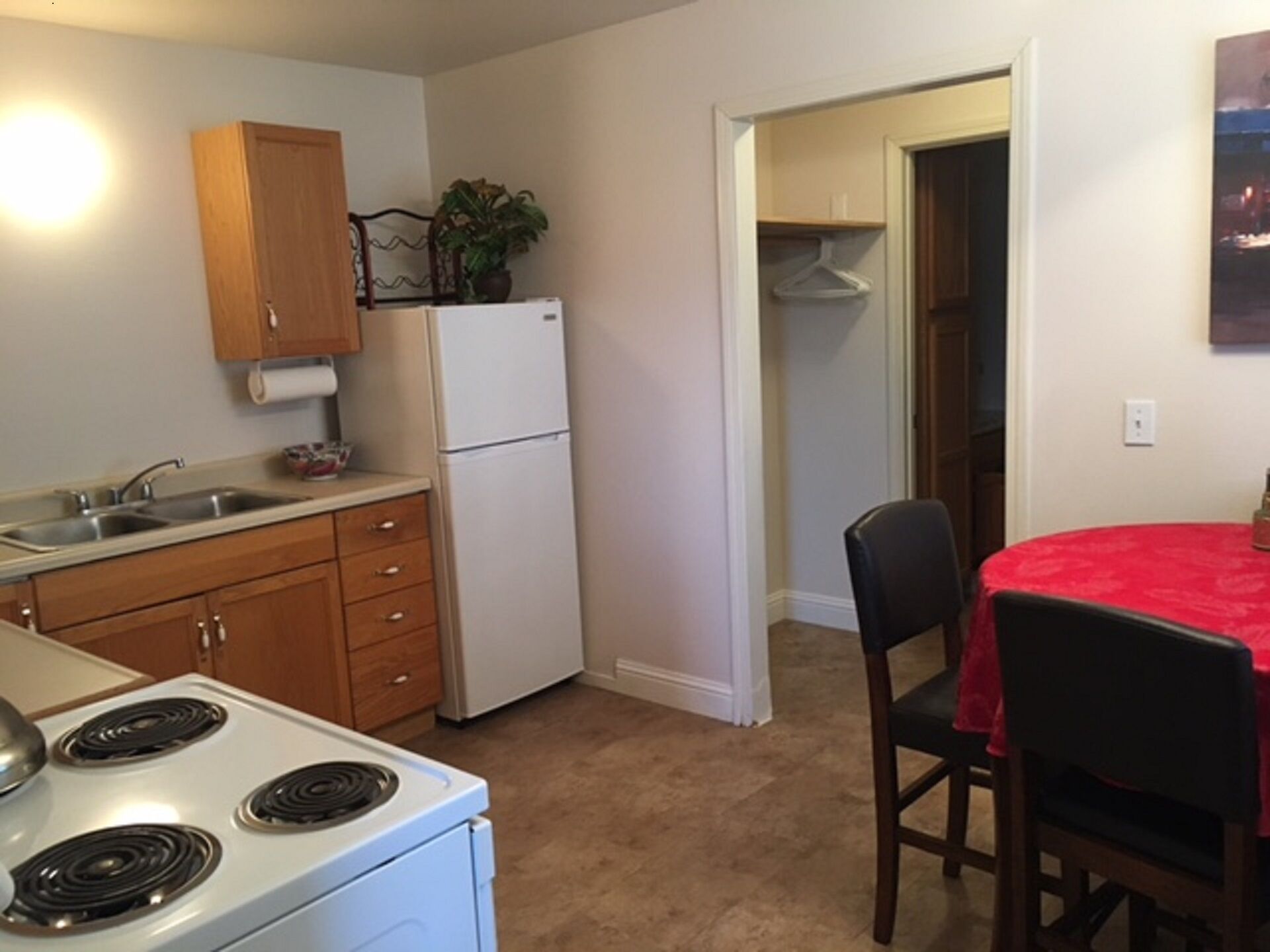 A compact kitchen with a stove, sink, and cabinets, leading to a dining area with a table and chairs.