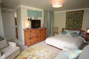 Un dormitorio con cama, cómoda, televisor, silla y un tapiz.