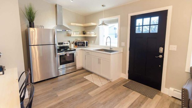 A modern kitchen with stainless steel appliances, white cabinetry, and a black door.