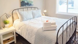 A bedroom with a bed, a nightstand, a lamp, a ceiling fan, a window, and a painting on the wall.