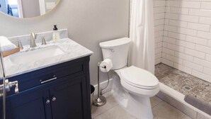 A modern bathroom with a white toilet, a dark vanity, a shower with a white curtain, and a mirror with a gold frame.