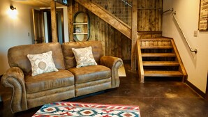 A cozy living room with a brown leather sofa, a patterned rug, and a wooden staircase. - Bitterroot Bunkhouse (Hamilton)