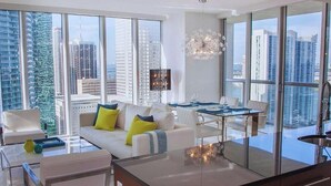A modern living room with a sofa, chairs, and a dining area with a table and chairs. Large windows offer a view of the cityscape. - Open-Concept Brickell Retreat | Walk to Everything (Miami)