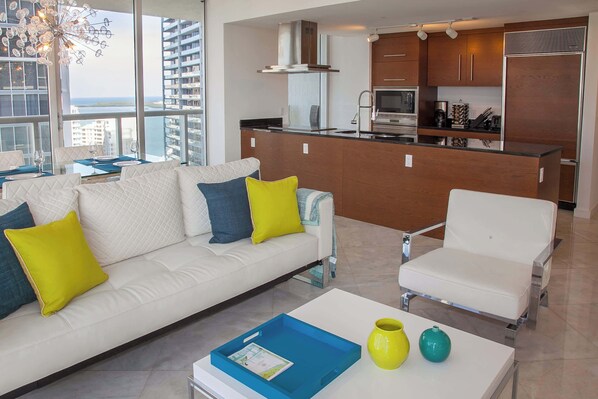 A modern living room with a white sofa, a white armchair, and a coffee table with a blue tray and two vases.