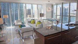 A modern living room with a sofa, coffee table, and dining area with a view of tall buildings. - Open-Concept Brickell Retreat | Walk to Everything (Miami)