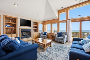 A spacious living room with a fireplace, large windows, and a view of the ocean.