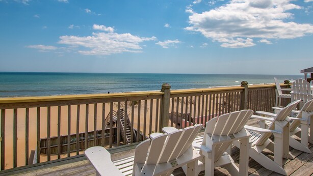 Une terrasse en bois avec des chaises blanches donnant sur une plage.