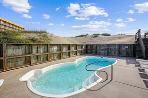 Une piscine entourée d’une clôture en bois, avec une terrasse en béton et un bâtiment visible au fond.