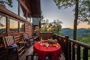 Une terrasse en bois avec une table rouge dressée pour le dîner, offrant une vue sur un paysage montagneux.