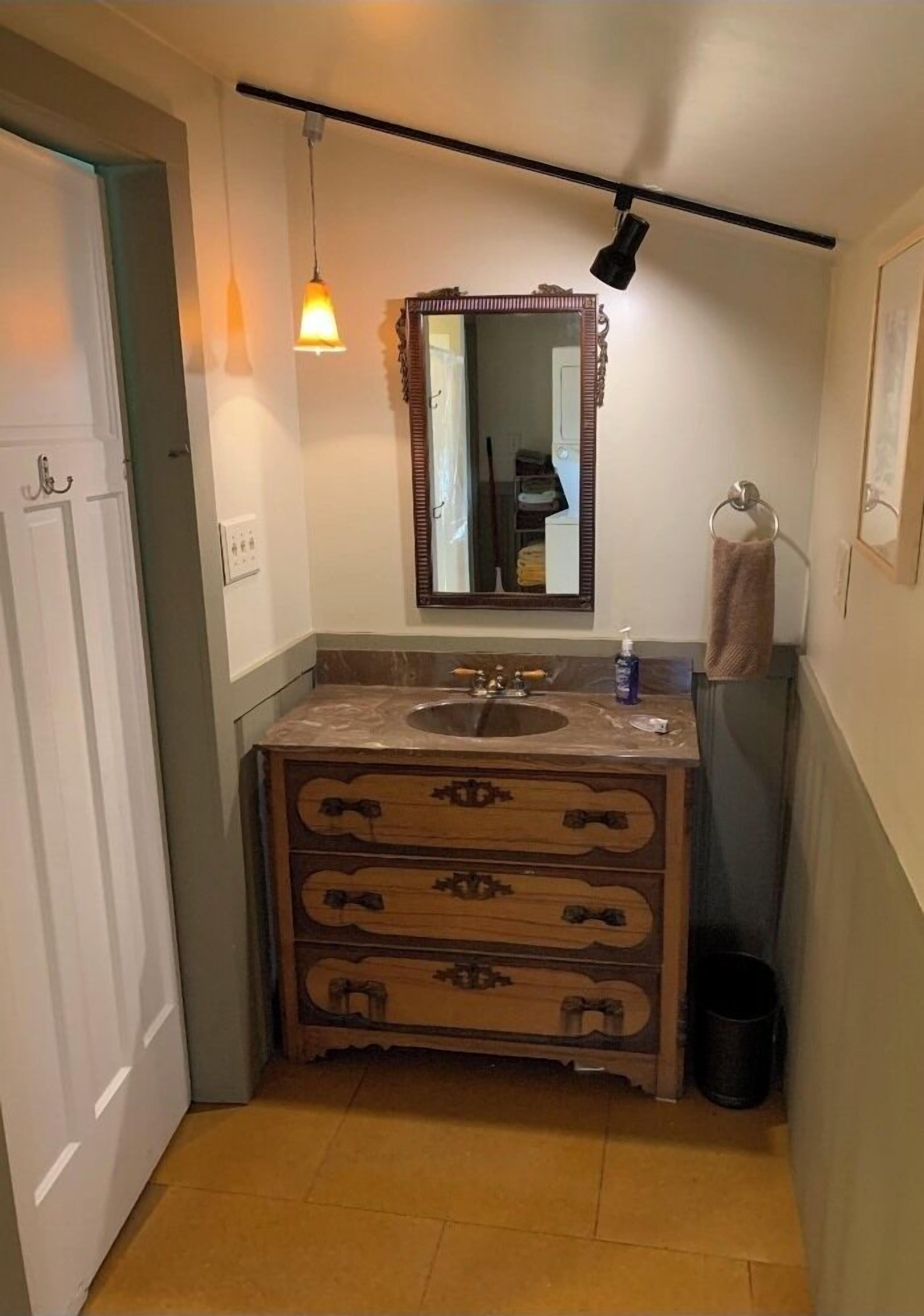 A compact bathroom with a wooden vanity, a sink, a mirror, and a hanging light fixture.
