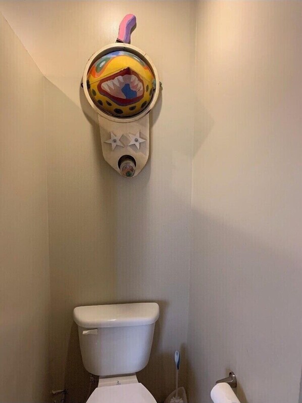 A toilet with a colorful, abstract decoration above it.
