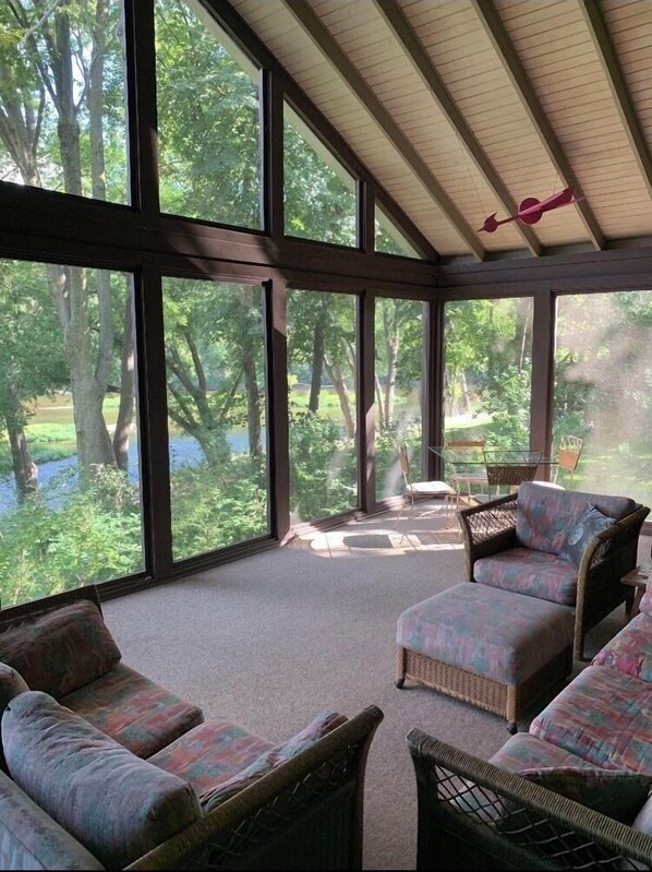 Relax in a serene outdoor space with a view of the surrounding landscape, featuring wicker furniture and large windows.