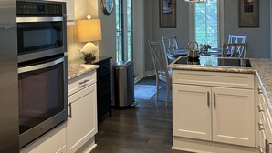 A modern kitchen with white cabinetry, stainless steel appliances, and a dining area with a chandelier. - Immaculate, 193 5-Star Reviews, Amazing Views, Updated, Pool heated/cooled (Hilton Head Island)