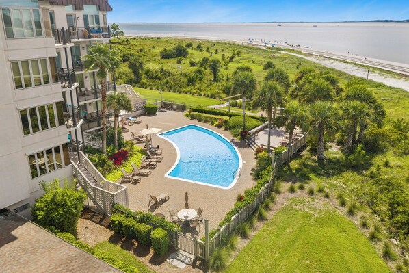 A pool surrounded by a landscaped garden with a view of the beach.