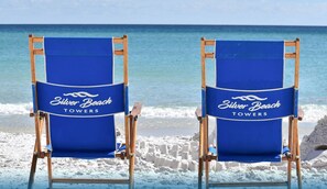 Zwei Liegestühle mit dem Schriftzug "Silver Beach Towers", auf einem Sandstrand vor dem Hintergrund von Wellen.