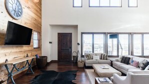 Un ampio soggiorno con una grande TV, elementi in legno, un tappeto in pelle nera e un divano con vista panoramica da ampie finestre.