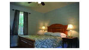 A bedroom with a wooden bed, two bedside lamps, a window with curtains, and a ceiling fan. - Gabouri Place ~ Completely Renovated Victorian in Ste. Genevieve's Historic Dist (Ste. Genevieve)