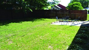 A backyard with a grassy lawn, a wooden fence, and a patio area with chairs and a table. - Gabouri Place ~ Completely Renovated Victorian in Ste. Genevieve's Historic Dist (Ste. Genevieve)