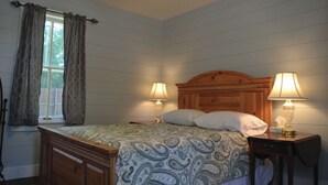 A bedroom with a wooden bed, two bedside lamps, a window with curtains, and a ceiling fan.