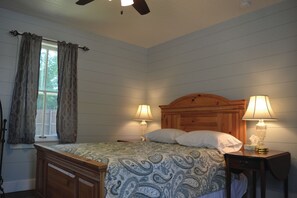 A bedroom with a wooden bed, two bedside lamps, a window with curtains, and a ceiling fan.