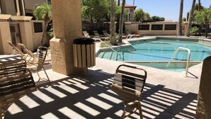 A pool area with lounge chairs and a table, surrounded by palm trees and a building with a number 39 sign. - Gated Community, Poolside, Newly Remodeled 2bed Condo (Phoenix)